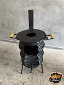 Fogão a lenha artesanal preto com alças amarelas e toalha, sobre chão de concreto cinza