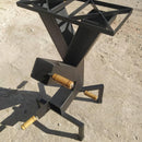 Suporte metálico preto para fogão com alças de madeira, sobre chão de terra