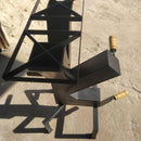 Espalhador de carvão em metal preto com alças de madeira sobre chão de concreto