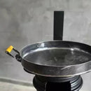 Panela de ferro fundido com alça amarela sobre fogão preto em ambiente cinza